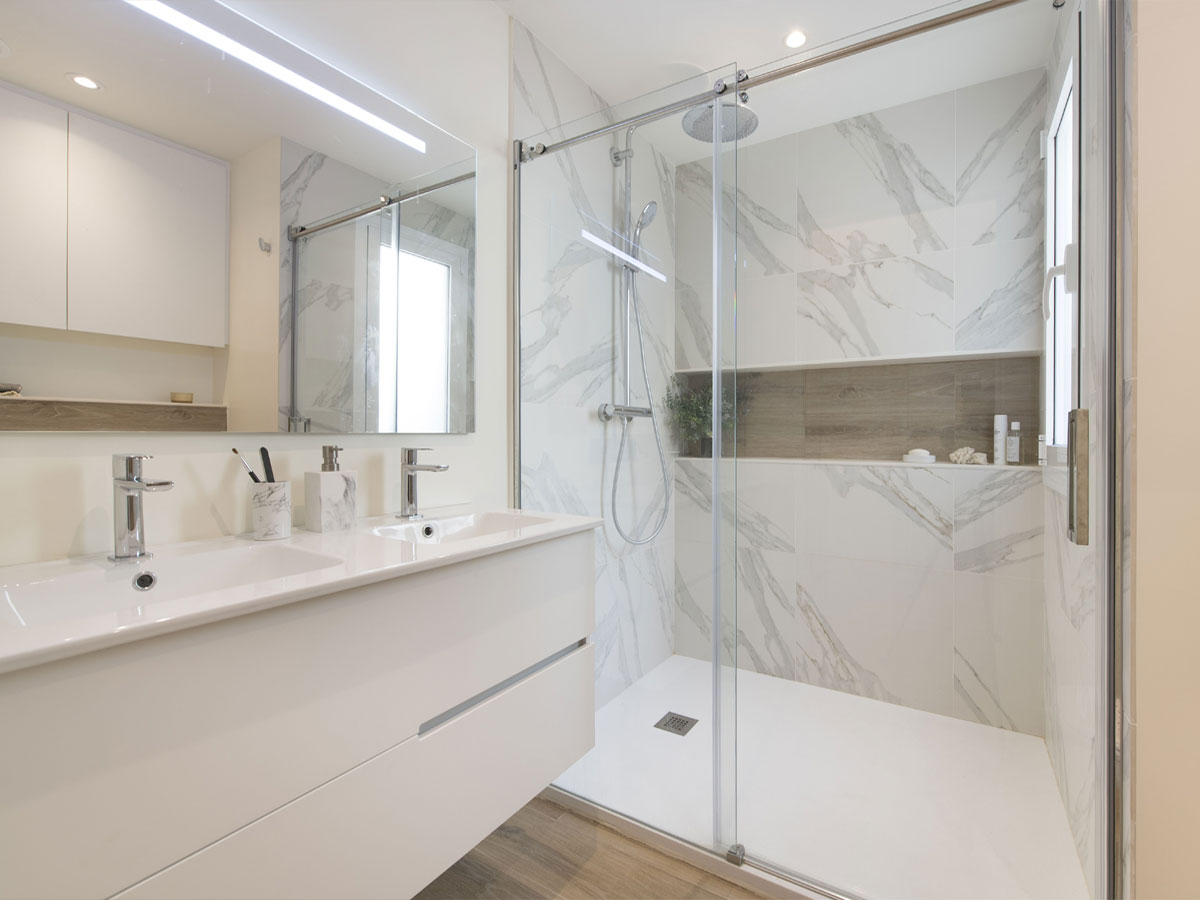 Baño reformado con ducha, mueble suspendido y revestimientos claros